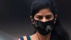 woman wearing a protective face mask walks along a street in smoggy conditions in New Delhi on November 4, 2019