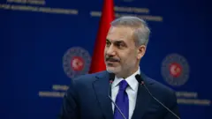 Hakan Fidan mavi kravat taktığı bir takım elbisesiyle mikrofonların arkasında basın açıklaması yapıyor