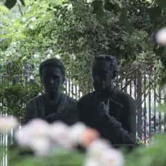 Duas esculturas, de um homem e uma mulher, em meio a flores