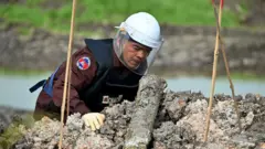 Un démineur du Centre cambodgien d'action contre les mines examine une munition non explosée dans la province de Svay Rieng, au Cambodge.