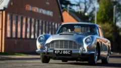 John and Susan Williams driving in their restored Aston Martin outside the factory where it was built