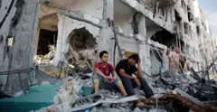 طفلين من غزة يجلسان أمام بيتهما المدمر