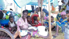 Umugore w'impuzi ariko aratora umuceri akikujwe n'abana ku kibuga c'umupira ca Rugombo aho yahungiye mu ntara ya Cibitoke