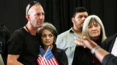 A man and a woman hugging holding American flags with stern expressions