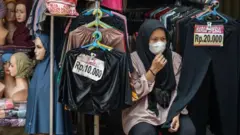 Seorang penjual pakaian menunggu pembeli yang tak kunjung datang di Pasar Jatinegara, Jakarta, pada Juli 2024. 