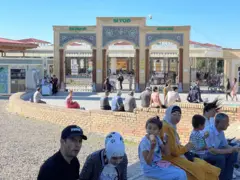 Siyob bozor kirishida odamlar bolalari bilan o'tiripti. Bolalar muzqaymoq yemoqda.