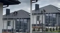 На кадрах із відео видно, як чоловік із іншим чоловіком у формі б'ються на даху, а потім падають разом, і там їх допомагає зловити інший чоловік