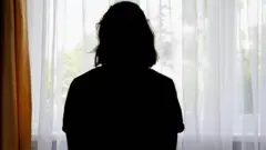 Tül perdesi çekilmiş bir pencereden dışarı bakan bir kadının arkadan görüntüsü 