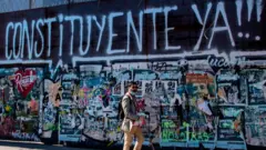 Un hombre junto a un mural con un graffiti a favor de la Constituyente en Chile.