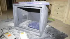 Imagem de um cofre que teve a porta arrombada sobre um tapete, com poeira espalhada por toda parte, e o que parece ser mobília de quarto de cor creme com gavetas embutidas ao fundo. Dentro do cofre e espalhados em volta, encontram-se pastas e papéis, além de objetos como um cabo de computador. Aparentemente, houve objetos removidos.