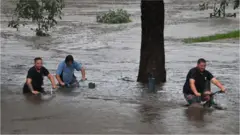Three men push bikes through waist-deep water