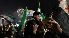 Мальчик сидит на плечах у взрослого на фоне сирийского флага и фейерверков