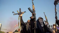 Mulheres seguram rifles durante uma manifestação pró-governo do Dia do Exército Nacional, em 17 de abril de 2026, em Teerã, Irã. Em 8 de abril, o presidente dos EUA, Donald Trump, anunciou um cessar-fogo de duas semanas entre os EUA e o Irã. As negociações de paz, facilitadas pelo Paquistão, ainda não produziram uma solução duradoura, sendo as principais questões pendentes as capacidades nucleares do Irã e o controle do Estreito de Ormuz.