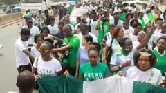 Awọn oluwọde to wọ asọ alawọ eweko ati funfun wa loju popo, wọn gbe akọle lọwọ lati tako titẹ ẹtọ ọmọniyan loju.