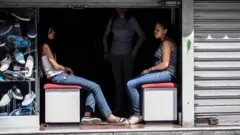 Funcionárias de uma sapataria sentadas na entrada de uma loja às escuras, durante um corte de eletricidade em Caracas