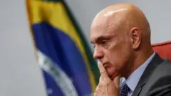 Alexandre de Moraes: as principais controvérsias do ministro nos últimos anos 4 Alexandre de Moraes, um homem branco calvo, de terno e semblante sério, com olhar pensativo