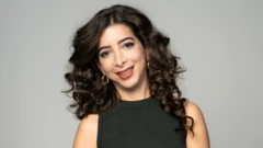 Uma mulher de cabelos pretos e cacheados, usando regata preta e brincos de argola dourados