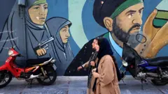 Sokakta vatansever bir duvar resmi önünden geçen başörtülü şık kadınları görüyoruz. Duvar resminde muhafazakar iki kadından biri silah tutuyor.