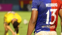 Vista de costas de Edgar Medrano, atacante do FAS, em primeiro plano. Na sua camisa, pode-se ler seu sobrenome e o número 13. Ao fundo, no campo, outro jogador vestido de amarelo aparece desfocado.