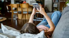 一名少女在家中躺在沙發上滑手機並瀏覽社交媒體。