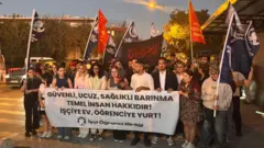 Cevizlibağ Kız Öğrenci Yurdu önünde eylem yapan öğrenciler "Güvenli, ucuz, sağlık barınma temel insan hakkıdır" yazılı pankartla duruyor.