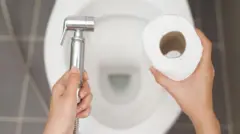 Bir kadın bir elinde taharet musluğu diğerinde tuvalet kağıdı tutuyor