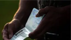 Aworan to ṣafihan ọwọ to mu iwe irinna dani, o ṣi iwe naa, fọto han nibẹ pẹlu awọn alaye nipa ẹni to wa ninu fọto ọhun. 