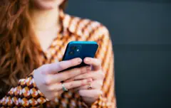 هاتف ذكي يُقرأ، تحمله امرأة ذات شعر أحمر طويل ومموّج، ترتدي قميصاً بنقشات باللونين البني والبرتقالي، إلى جانب الأبيض والأحمر.