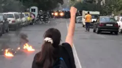 A young woman without a headscarf raises a fist at a protest in Iran sparked by the death of Mahsa Amini