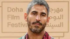 صورة للصحفي الكويتي الأمريكي أحمد شهاب الدين ويظهر في الخلفية شعار مهرجان الدوحة السينمائي