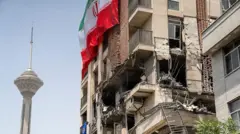 Una bandera iraní ondea en un edificio dañado durante los recientes ataques israelíes cerca de la Torre Milad en Teherán