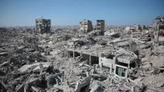 Foto panorâmica mostrando a devastação em Gaza. Prédios demolidos e escombros são visíveis.