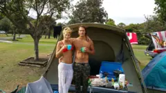 Alex e Ellidy abraçados em frente a uma barraca de acampamento