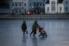 Família patinando no gelo, com casas em bom estado ao fundo
