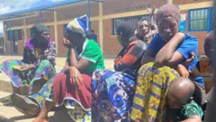 Abagore bacyenyeye ibitege bicaye hasi bari kumwe n'abana bato.