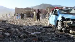 ساکنان روستایی در ولسوالی سمکنی پکتیا در کنار بقایای ساختمانی که در پی حمله هوایی دیشب پاکستان تخریب شده است، ۲۹ ژوئن ۲۰۲۶