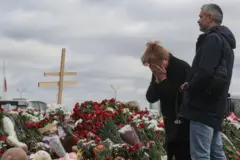 Woman covers her face as she next to a man in front of floral tributes at a memoral for victims of Crocus City Hall attack in Moscow, 25 March 2024 