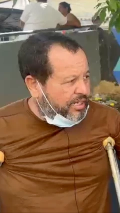 Un hombre con muletas, tiene barba y camisa marrón