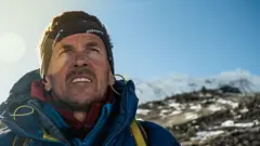 Davorin Davo Karničar gleda uvis sa planinskim vrhovima iza sebe 