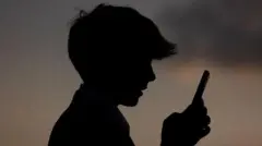 پرهیب یک پسر نوجوان که موبایلی در دست نگاه می‌کند