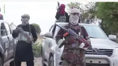 Agbebọn mẹta ti wọn gbe ibọn dani, duro nibi ọkọ meji, bo oju wọn
