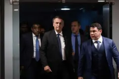 Bolsonaro caminha entre outros homens com olhar sóbrio