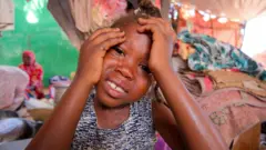 Foto de uma criança sudanesa chorando com as mãos no rosto.