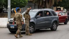 複数の女性が乗った乗用車に向かって、迷彩服姿の兵士たちが手で方向を示している。