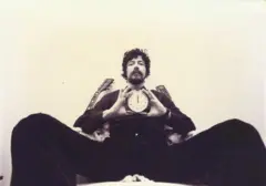 Raul Seixas sentado mostrando relógio com as mãos