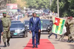 Faure Gnassingbé, le chef de l'Etat togolais passant en revue une troupe avec des véhicules en arrière-plan