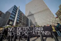Pessoas seguram uma faixa de protesto preta contra a detenção e deportação de imigrantes em frente a dois edifícios