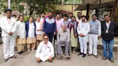 
රෝහල් කාර්ය මණ්ඩලය සමග රෝද පුටුවක සිටින 'ශිවම්'