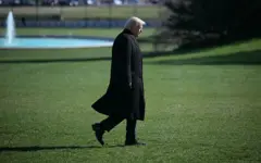 Donald Trump camina por la grama de la Casa Blanca con una gran gabardina negra