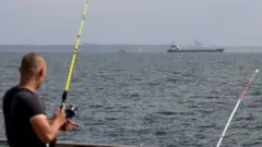 A fisherman watches the ship leave port